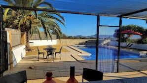 Un espace aménagé au bord de la piscine, avec un patio couvert, des sièges d’extérieur et une vue sur la piscine.