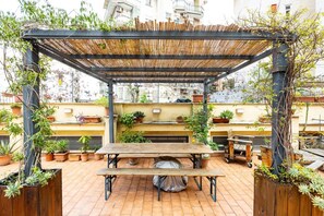 Une terrasse sur le toit avec une table en bois et des bancs, entourée de plantes en pot et d’une pergola en bambou.