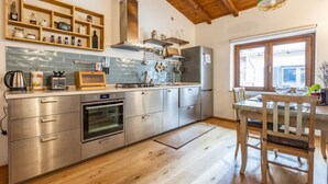 Uma cozinha moderna com eletrodomésticos de aço inoxidável, prateleiras de madeira e uma mesa de jantar de madeira.