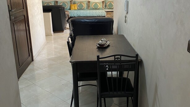 A dining area with a table and chairs, a sofa with patterned cushions, and a tiled floor.
