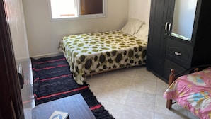 A bedroom with a bed, a wardrobe, a window, and a small table.