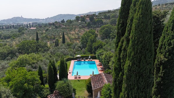 A pool surrounded by greenery and a hilltop view.