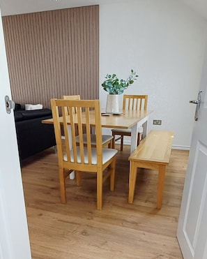 A dining area with wooden furniture, a potted plant, and a black sofa.