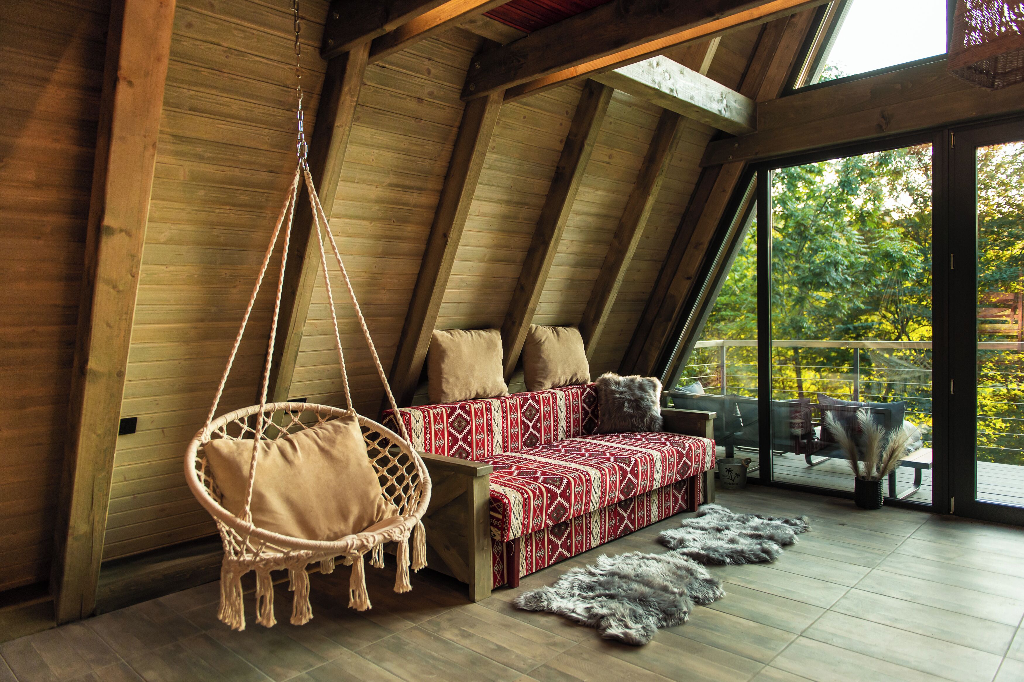 A wooden interior with a hanging chair, a patterned sofa, and a view through a glass door.