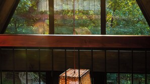 Ein dreieckiges Fenster mit hereinströmendem Sonnenlicht, ein Holzbalken und eine hängende Leuchte.