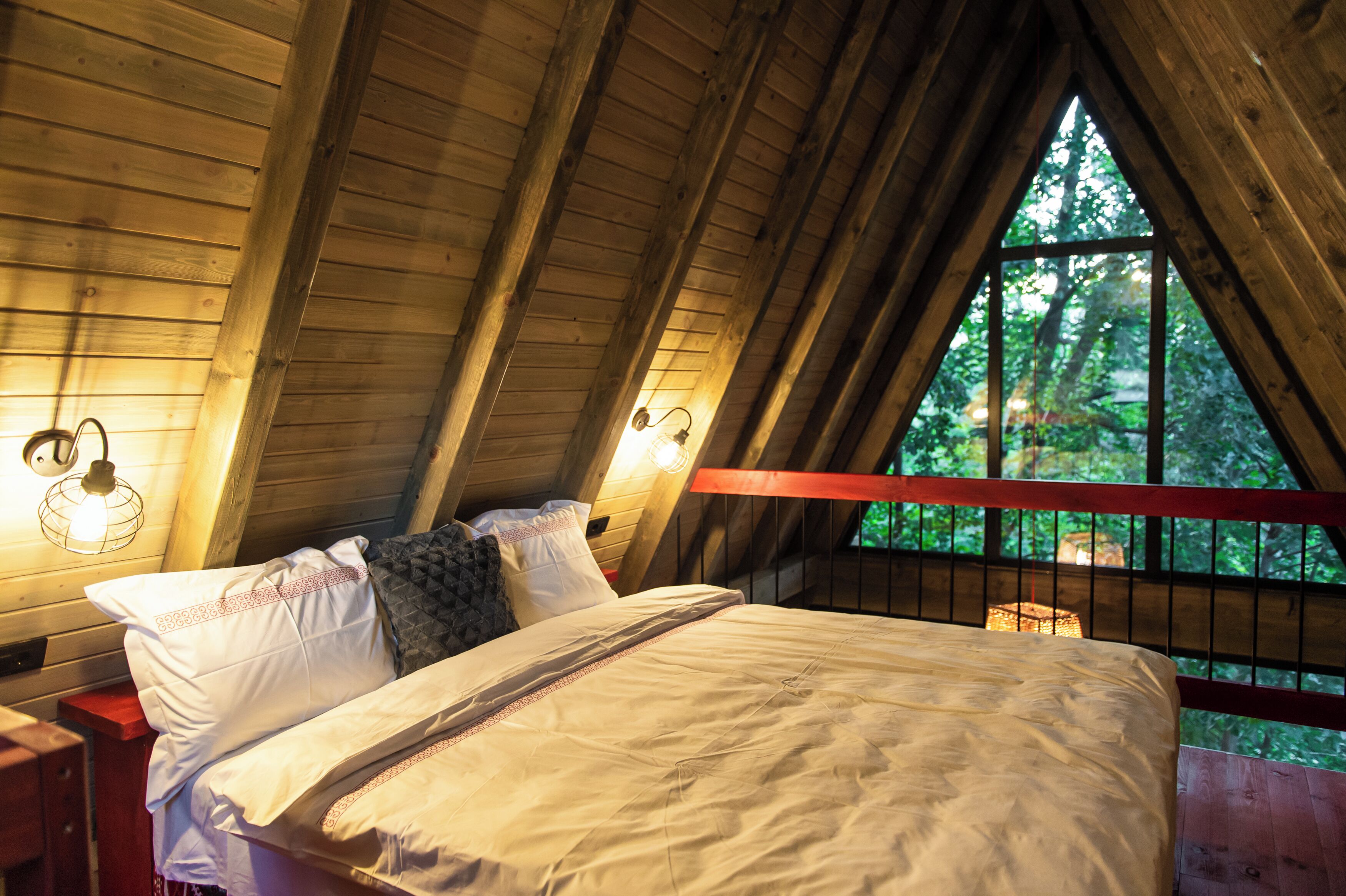 Een slaapkamer met een houten plafond, een bed met witte beddengoed en een raam met uitzicht op bomen.