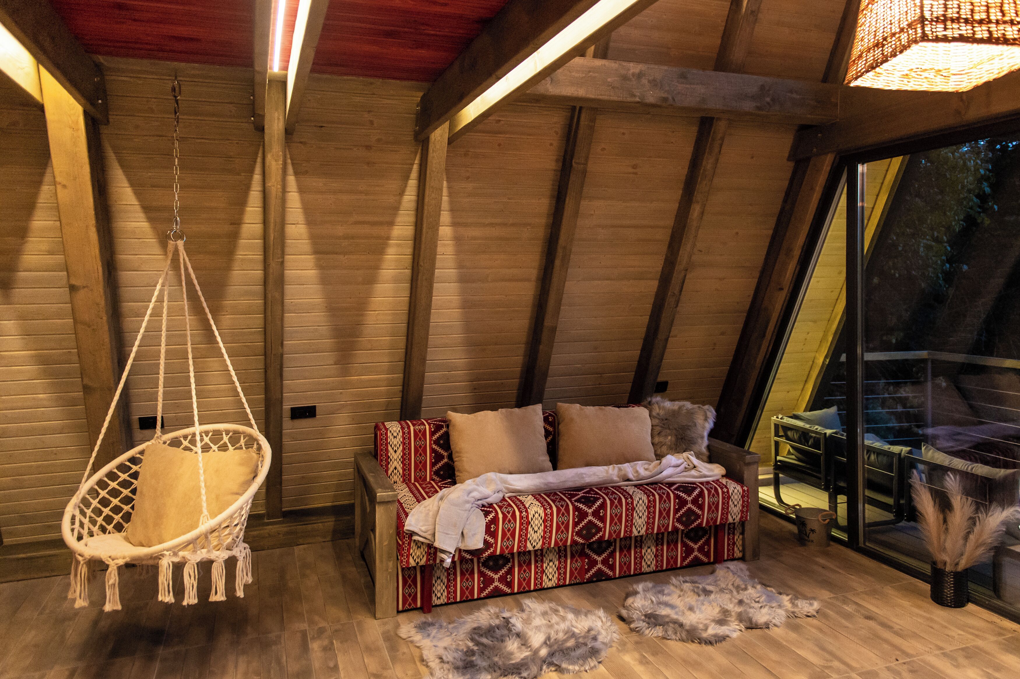 A cozy room with a hanging chair, a patterned sofa, and a view through a large window.