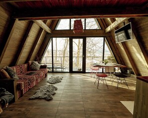 A high-ceilinged room with a sloped ceiling, a large window, a sofa, a dining table with chairs, and a television. - Hai la Munte Bran (Bran)