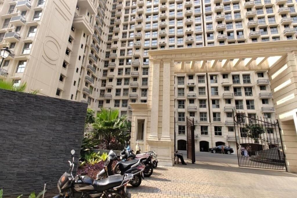 A multi-story residential building with a gated entrance, a parking area, and a row of parked motorcycles.