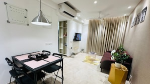 Een moderne woonkamer met een eethoek, een flatscreen televisie, een plafondventilator en een groot raam met gordijnen.