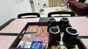 Een eethoek met een tafel voor vier personen, voorzien van zwarte mokken en een dienblad met kleurrijke servetten en koffiehoeveelheden.