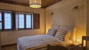 Un dormitorio con una cama grande, cabecera de madera, dos lámparas de noche y un ventanal con cortinas.