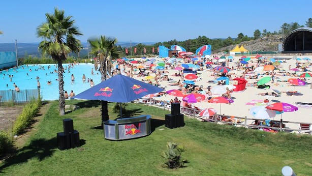 Una playa con piscina, palmeras y sombrillas con la marca Red Bull.