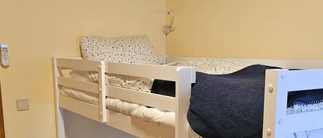 A bunk bed room with a wooden ceiling, a bedside table with a lamp, and a power outlet on the wall.