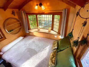 A cozy room with a bed, a window with a view, a wall-mounted shelf, and a dreamcatcher.