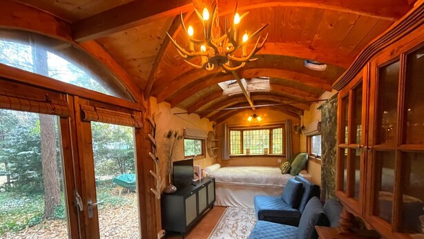 A cozy cabin interior with a large bed, a sofa, a desk, and a chandelier.