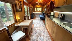 A cozy cabin interior with a long dining table, a sofa, and a kitchen area with wooden cabinets and a sink.