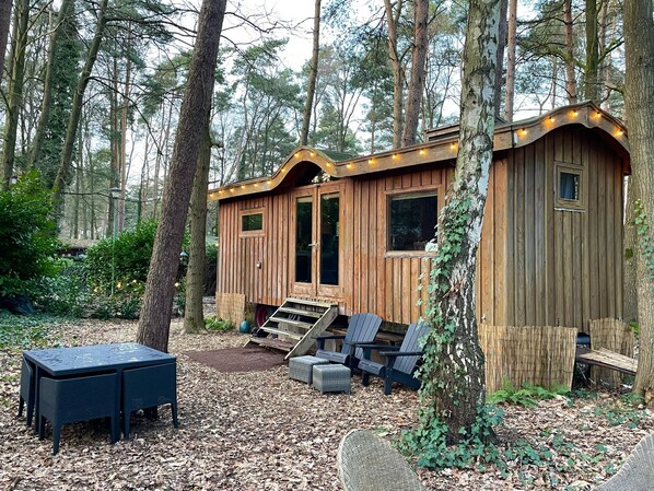 A wooden cabin with a porch, outdoor seating, and a small window.