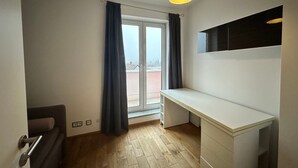 Una habitación con puerta corrediza de vidrio, un escritorio blanco, una lámpara de techo y vistas al exterior.