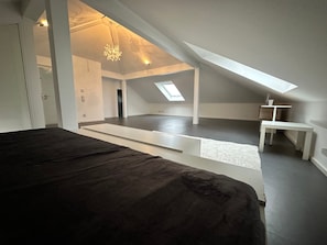 A spacious attic bedroom with a skylight, a large bed, and a small table.