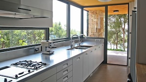 A modern kitchen with a gas stove, sink, and large windows offering a view of greenery. - Luxury Seafront Villa • Infinity Pool - Walk to Beach (Tarragona)