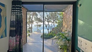 A bedroom with a view of a stone pathway leading to a body of water, a bed, and a large window with curtains. - Luxury Seafront Villa • Infinity Pool - Walk to Beach (Tarragona)