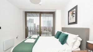 Ett modernt hotellrum med en stor säng, utsikt genom en skjutdörr, ett inramat konstverk på väggen och ett sängbord med en lampa.