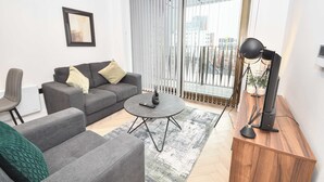Ett modernt vardagsrum med en grå soffa, ett runt soffbord och ett träbord med en lampa.