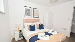 Une chambre d’hôtel bien rangée, avec un lit, une table de chevet, une lampe et une œuvre d’art encadrée au mur.