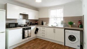 Una cucina moderna con mobili bianchi, forno a microonde, piano cottura, forno e lavatrice.