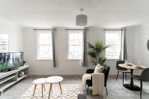 Un salon moderne doté d’un téléviseur à écran plat, d’une table à manger avec des chaises, d’un canapé et d’une grande fenêtre avec des rideaux.