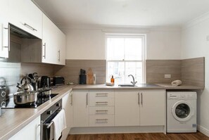 A modern kitchen with white cabinets, a built-in oven, a stove, and a washing machine.