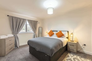 A bedroom with a bed, bedside table, lamp, and a window with curtains.