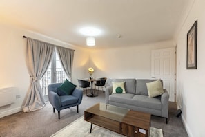 A modern living room with a grey sofa, a blue armchair, a glass coffee table, and a dining table with chairs.