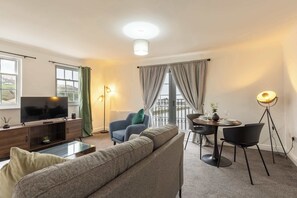 A living room with a sofa, a TV, a dining table with chairs, a floor lamp, and a balcony with curtains.