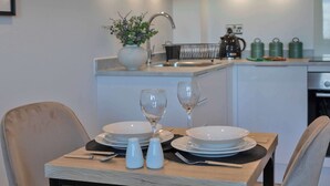A modern kitchen with a dining area, featuring a wooden table set for two, a sink, and a kettle. - Fabulous 1 Bedroom Apartment in Gravesend Centre (Gravesend)