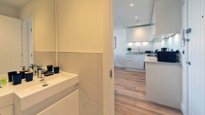 A modern bathroom with a large mirror and a vanity with toiletries. The adjacent kitchen has white cabinets and a microwave. - Fabulous 1 Bedroom Apartment in Gravesend Centre (Gravesend)