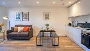 Ein modernes Wohnzimmer mit einer Couch, einem Esstisch für vier Personen und einer Küchenzeile mit Geräten.