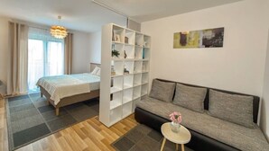 Ein stilvolles Zimmer mit Bett, Sofa, Bücherregal und einem kleinen Tisch mit Blumen.