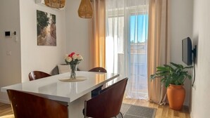 Ein stilvoller Essbereich mit einem weißen Tisch, braunen Stühlen, einer Vase mit Blumen und einem großen Fenster mit Vorhängen.