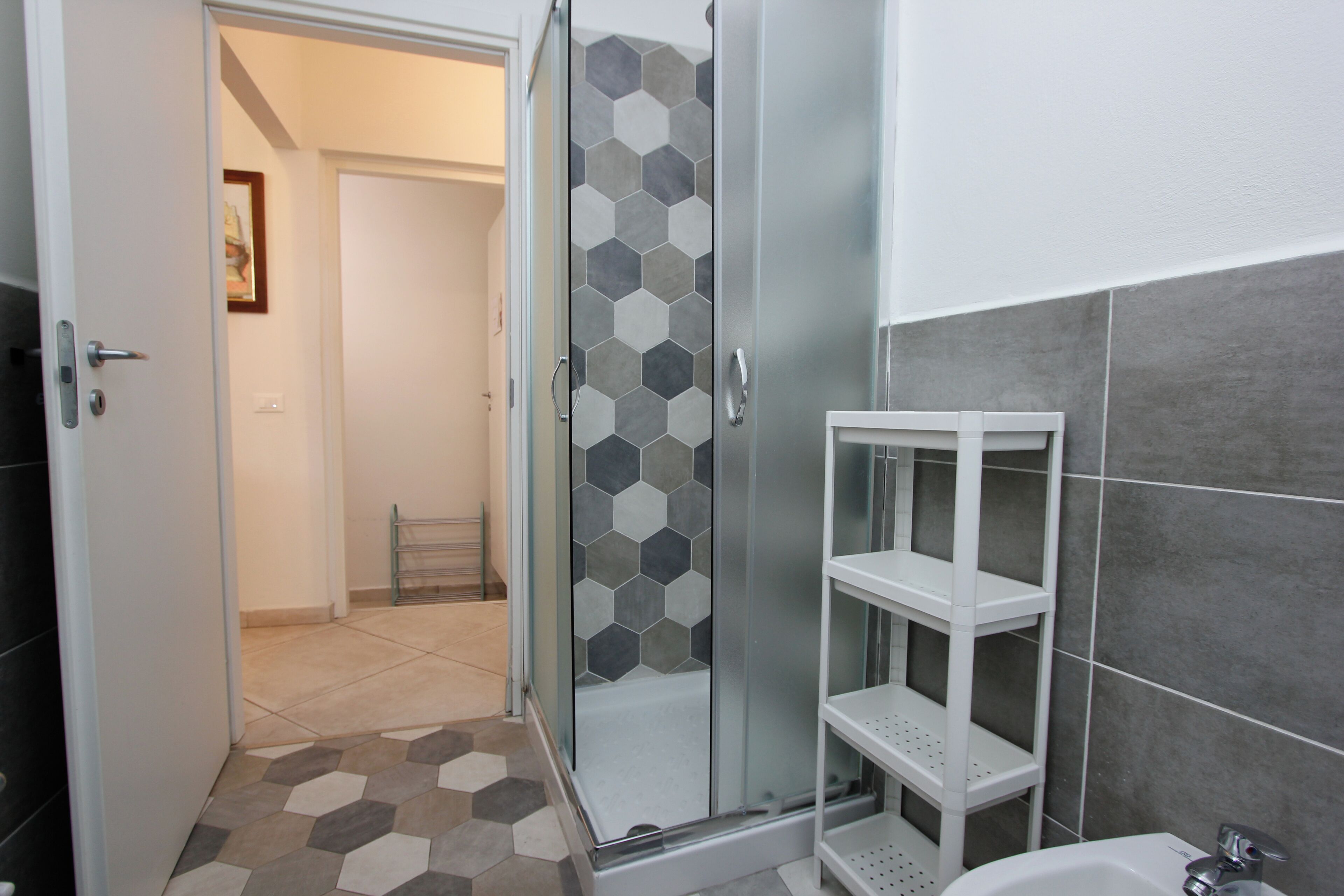 A modern bathroom with a glass shower enclosure, a white sink, and a tiled floor.