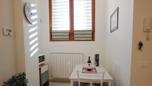 A small dining area with a white table, chairs, a potted plant, a clock, and a window with blinds. - Suite dei Vanni - Free private parking (Florence)
