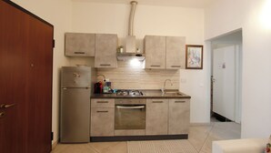 A compact kitchen with a built-in oven, a sink, and a refrigerator. There is a wooden door on the left and a white door on the right. - Suite dei Vanni - Free private parking (Florence)
