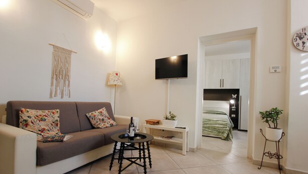 A living room with a sofa, a coffee table, a TV, and a bed in the background. - Suite dei Vanni - Free private parking (Florence)