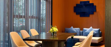 Un área de comedor moderna con una mesa redonda, cuatro sillas, un elemento decorativo azul en la pared y un sofá con cojines azules.