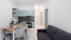 A modern kitchen with light blue cabinets, a dining table with chairs, and a dark grey sofa. - Apartment 'Casa Giuseppe Centro - Sanremo' with Sea View near Piazza Colombo (Sanremo)