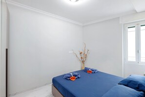Ein Schlafzimmer mit einem Bett, einer Vase mit Zweigen und einem Fenster.