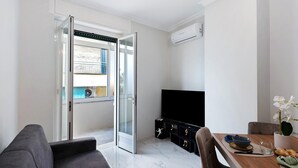 A modern living room with a sofa, a dining table with chairs, a TV, and a sliding glass door leading to a balcony. - Apartment 'Casa Giuseppe Centro - Sanremo' with Sea View near Piazza Colombo (Sanremo)