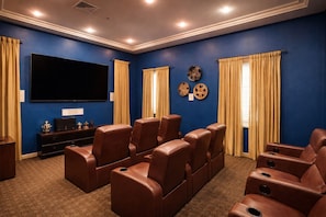 A home theater room with blue walls, brown leather recliner seating, a large flat-screen TV, and a small console table with decorative items. - MDR 1BA ESCAPE (Marina del Rey)
