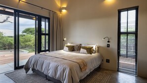 Quarto moderno com uma cama grande, vista para o verde lá fora e uma porta de correr de vidro.
